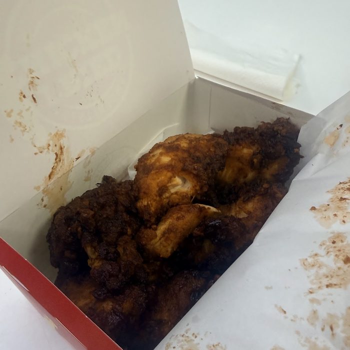 A box of dark, heavily sauced fried chicken pieces